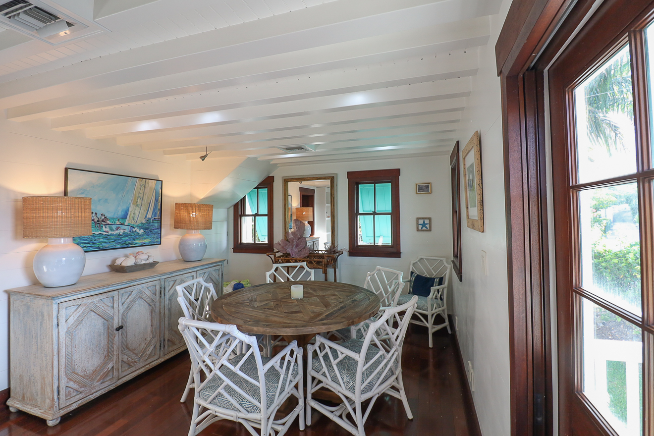 Cottage One dining room with round table, bamboo chairs, sideboard, and sailing artwork