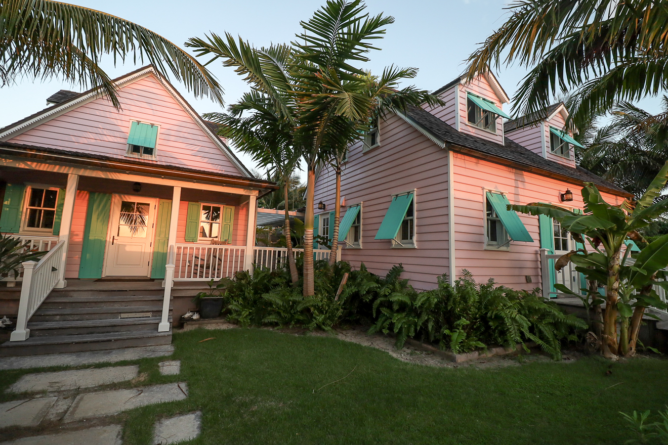 Twin pink cottages with teal shutters at golden hour, lush tropical garden